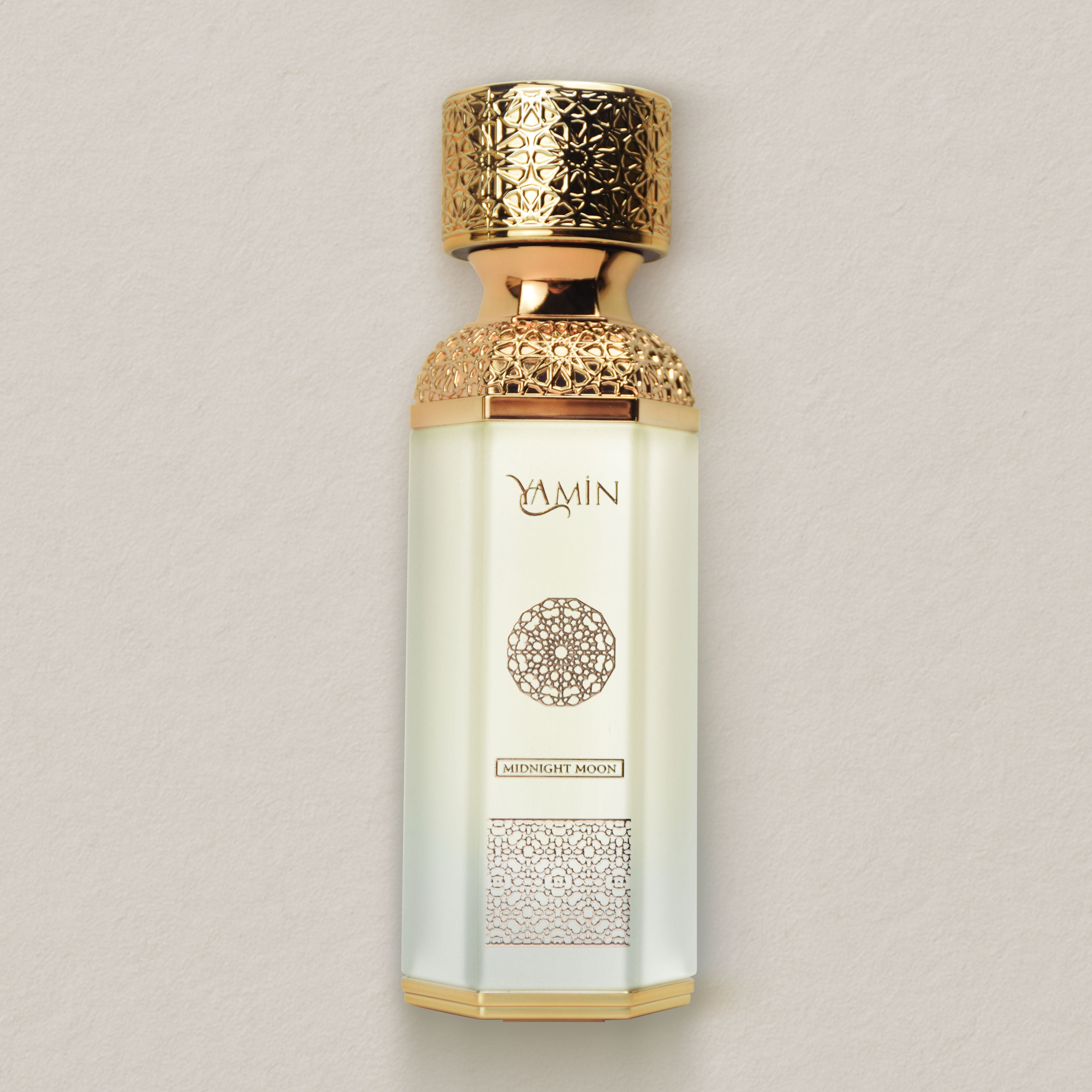 Yamin Midnight Moon perfume bottle with gold cap and intricate design on a beige background