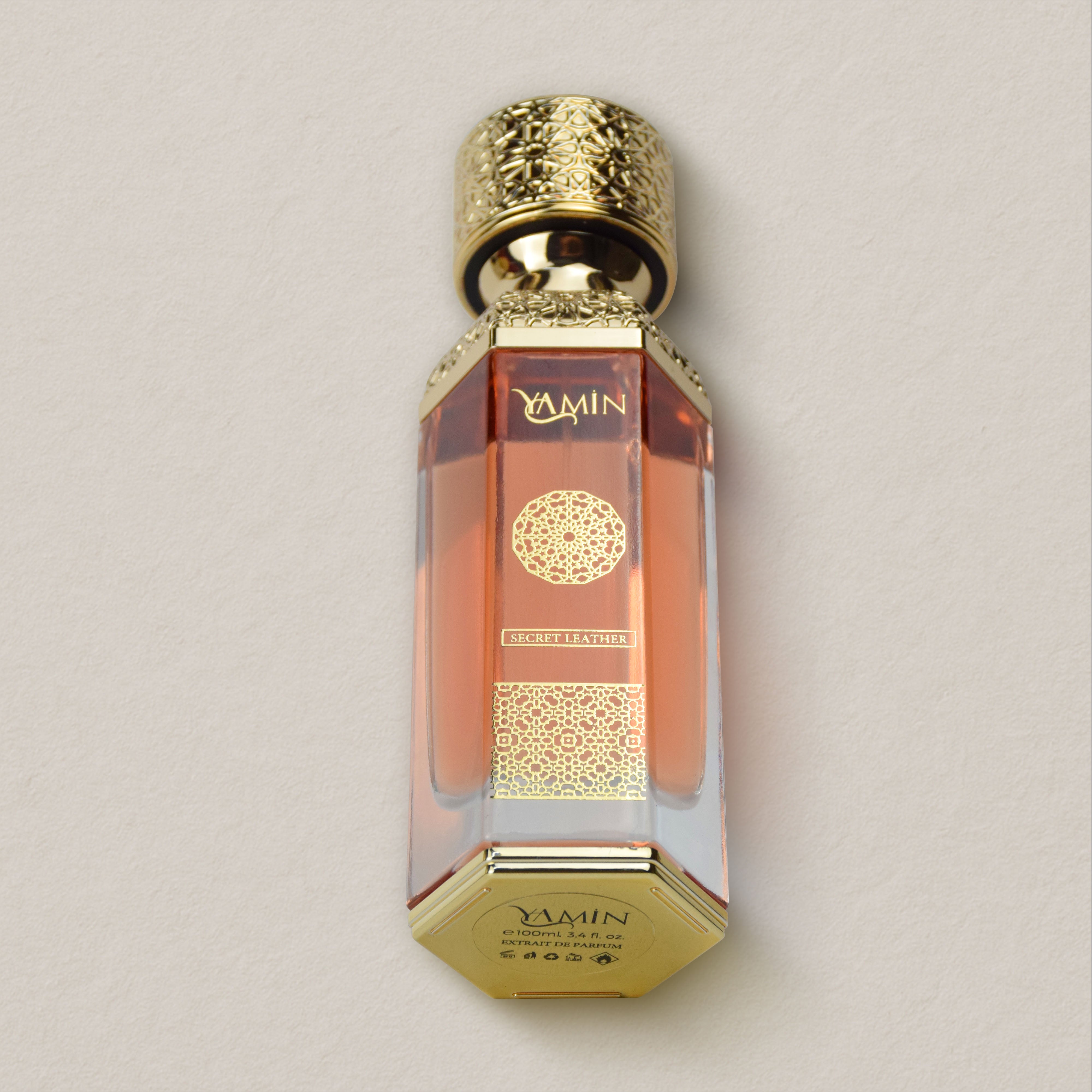 Yamin Secret Leather perfume bottle with gold cap and intricate design on a beige background